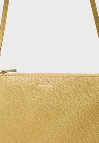 Texturált sárga bőr kézitáska sima cipzárzárral, finom, fehérben domborított logóval. Kompakt kialakítás vállpánttal.