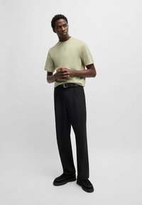 T-shirt verde chiaro a maniche corte, pantaloni neri su misura e scarpe nere chunky. Tessuto liscio con vestibilità rilassata, caratterizzato da un sottile logo.