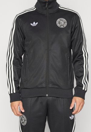 Zwarte Adidas trainingspak met witte strepen op mouwen en broek, met Deutscher Fussball-Bund-logo's op borst en dij.