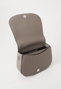 Brązowa torebka na ramię z syntetycznej skóry z zakrzywionym klapkiem, zapięciem na zatrzask i srebrnym okuciem. Wnętrze ma jedną przegrodę i detal z logo.