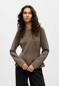 Rjava dolgosleeve majica s krožnim ovratnikom in rahlo razširjenim robom, izdelana iz gladkega blaga. Model jo nosi s črnimi hlačami.