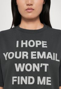 Grå bomulds T-shirt med stort hvidt tekst, der står: "JEG HÅBER DIN E-MAIL IKKE FINDER MIG." Korte ærmer og rund halsudskæring.