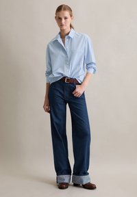 Lichtblauw gestreepte button-up shirt met lange mouwen, gecombineerd met donkere denim wijde broek en een bruine leren riem. Bruine hakken.