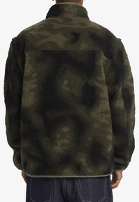 Chaqueta de forro polar con patrón de camuflaje, que cuenta con un cuello alto y una textura suave, en tonos de verde oscuro y negro. Incluye un dobladillo ajustable.