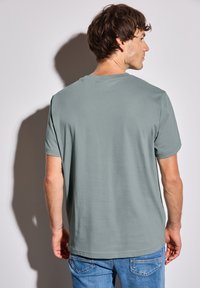 T-shirt vert à manches courtes en tissu doux, présentant un col rond classique et une coupe décontractée, associé à un jean bleu clair.