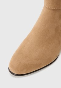 Bottine en daim marron avec un nez pointu et une texture lisse. Présente une semelle noire et des coutures discrètes le long du bord supérieur.