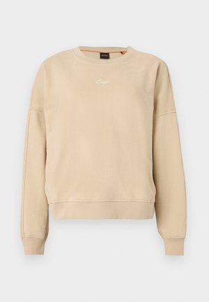 Beige long-sleeve crewneck sweatshirt with ribbed cuffs and hem, small white embroidered logo centered on the chest.