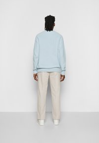 Helles blaues Crewneck-Pullover mit gerippten Bündchen und Saum, getragen zu beigen, locker sitzenden Hosen und weißen Sneakern. Strukturierter Strickstoff.