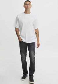 Hvid, kortærmet t-shirt med en tekstureret finish, parret med mørkegrå slim-fit jeans og sorte sneakers med hvide såler.