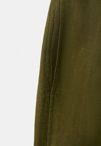 Gros plan sur un tissu vert olive avec une couture visible et un tissage texturé, mettant en valeur les détails de la couture le long du bord.