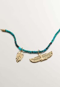 Collar de cuentas turquesas con colgantes en tono dorado: un símbolo de mano y una figura alada, destacando detalles e texturas intrincadas.