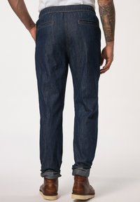 Jeans med elastisk midja, mörkblå färg, rak passform, uppvikta cuffs och två bakfickor. Bruna boots är på fötterna.