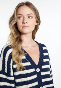 Cardigan a righe navy e crema lavorato a maglia con scollo a V, texture a coste e tre bottoni in evidenza sul davanti.