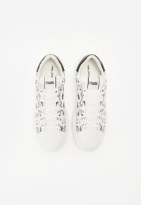 Bílé tenisky s černým grafickým vzorem, kulatou špičkou a šněrováním, s černým akcentem na patě a logem.