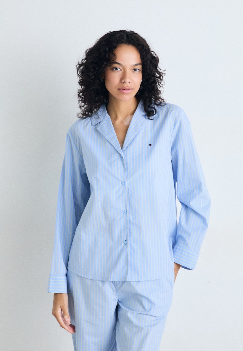 Blå och vitrandig pyjamasuppsättning som innehåller en skjorta med knappar och långa ärmar samt matchande byxor. Tillverkad av mjukt, lätt tyg.