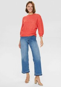 Maglione a maglia corallo con maniche larghe, abbinate a jeans a gamba dritta blu chiaro con orlo sfilacciato e sandali con tacco quadrato color sabbia.