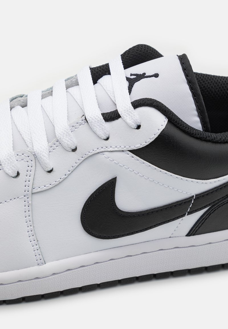 Weiße Leder-Sneaker mit schwarzen Akzenten, ausgestattet mit einem Swoosh-Logo, strukturiertem Gummisohle und flachen, weißen Schnürsenkeln. Klassisches Low-Top-Design.