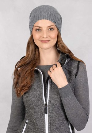 Grijze gebreide beanie met een geribbelde structuur, gedragen door een persoon; gecombineerd met een donkergrijze vest met rits en witte accenten.