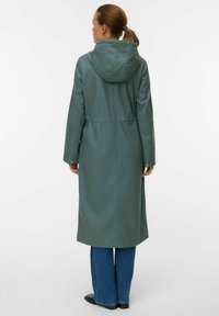 Lungo cappotto con cappuccio in verde tenue, realizzato in materiale liscio e impermeabile. Presenta una vita aderente e due tasche laterali, con una silhouette dritta.