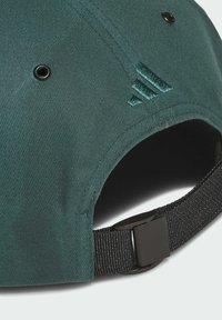 Gorra verde con tela texturizada, con ojales de ventilación negros y un logotipo bordado. Correa negra ajustable con cierre de plástico.