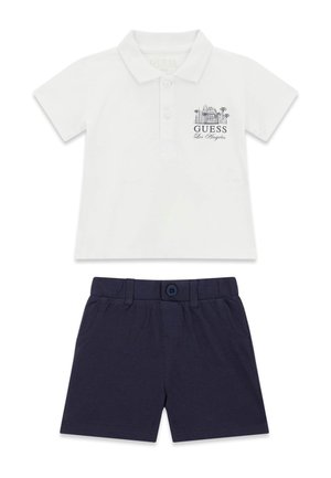 Polo bianco a maniche corte con la scritta "Guess Los Angeles" e grafica, abbinata a pantaloncini blu navy con bottoni frontali per bambini.