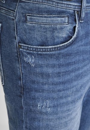 Jeans in denim con una lavatura blu medio, caratterizzati da una tasca posteriore con dettagli di cucitura e una leggera texture vissuta sul tessuto.