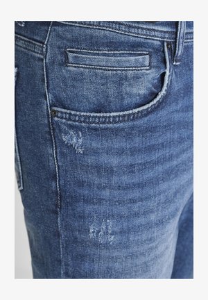 Jeans in denim con una lavatura blu medio, caratterizzati da una tasca posteriore con dettagli di cucitura e una leggera texture vissuta sul tessuto.