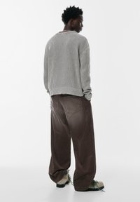 Grå ribbad tröja med sänkta axlar, bruna vida kordflöjtsbyxor och texturerade grå skor med gröna accenter. Bakvy.