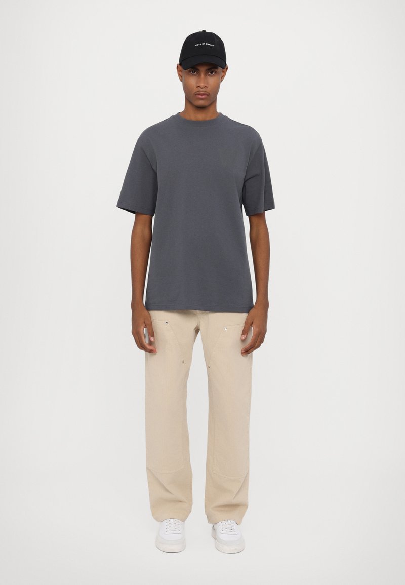 Gray short-sleeve t-shirt, beige loose-fit pants, and white sneakers. Black cap with embroidered text. Simple and minimalistic design.
