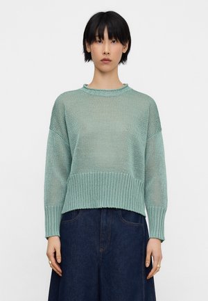 Hellgrüner Strickpullover mit lockerem Sitz, geripptem Halsausschnitt und Saum, lockeren Ärmeln und einer strukturierten Oberfläche. Kombiniert mit einem dunkelblauen Jeansrock.