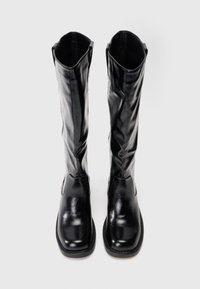 Botas negras de charol hasta la rodilla, con punta cuadrada y textura suave, con costuras mínimas y sin herrajes visibles.