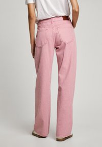 Rosa och vita randiga vida jeans med bakfickor och en brun läderlapp vid midjan. Slät bomullstextur.