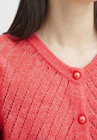 Cardigan lavorato a maglia di un vivace corallo, con un motivo a diamante testurizzato e ampi bottoni rossi lucidi sul collo davanti.