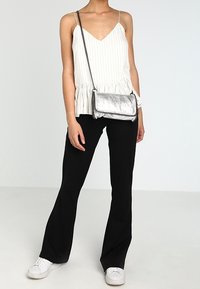 Biały prążkowany top bez rękawów z baskinką, zestawiony z czarnymi rozszerzanymi spodniami oraz srebrną metaliczną torebką na łańcuszku z ozdobnymi ćwiekami.