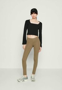 Top cropped preto de manga longa com decote quadrado, combinado com leggings verde-oliva e ténis cinzentos; inclui um boné de beisebol.