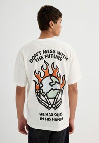 Camiseta de algodón blanca con un gran gráfico en la parte posterior que presenta llamas, un globo y texto en negrita negra y naranja. Mangas cortas.
