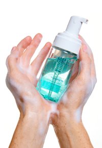Duidelijke schuimende micellar cleanser in een doorzichtige pomp fles, met turkoois vloeistof, vastgehouden in zeepachtige handen met een glanzende afwerking.