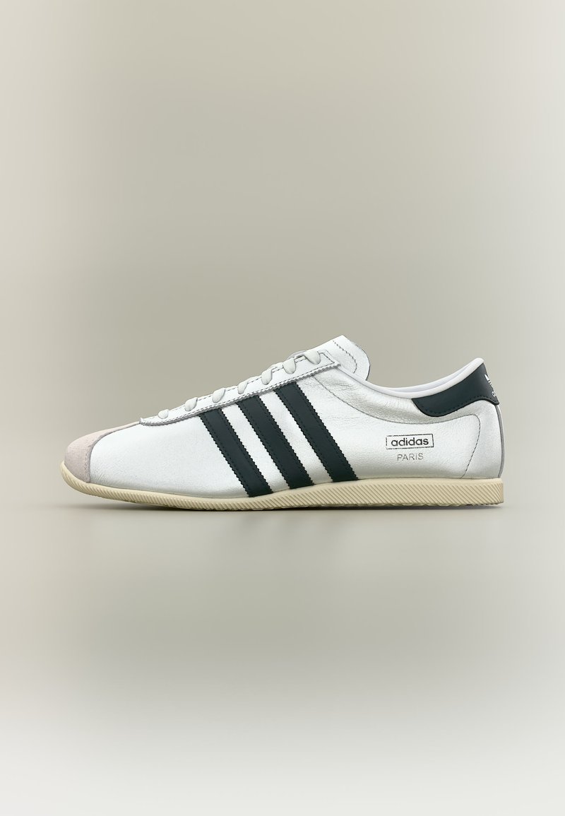 Λευκό αθλητικό παπούτσι Adidas Paris με μαύρες ρίγες, μπεζ σόλα και δερμάτινο κάλυμμα στα δάχτυλα, εμφανιζόμενο από το πλάι σε ουδέτερο φόντο.