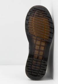 Semelle d'une botte en caoutchouc noir texturée avec des rainures horizontales antidérapantes et des sections translucides révélant la structure interne.