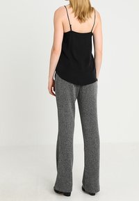 Svart kamisol med tunna axelband, i kombination med grå utsvängda byxor i strukturerad tyg med en melerat mönster.