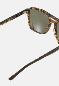 Braune Schildpatt-Sonnenbrille mit dunklen Gläsern, viereckiger Form und metallischen Akzenten an den Scharnieren. Robuste Kunststoffrahmen mit glatter Oberfläche.