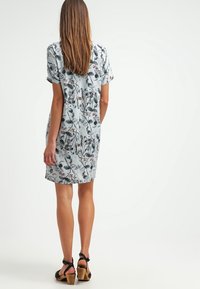 Kortärmad, ljusblå klänning med blommigt mönster. Har en lös passform och rak fåll, ihop med svarta remsandaler på en plan yta.
