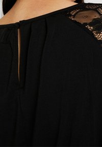 Czarna odzież z fakturowanym akcentem z koronki na ramieniu, z detalem w kształcie dziurki z tyłu oraz miękkim, zwiewnym materiałem.