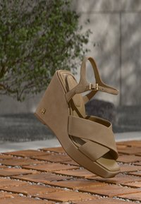 Μπεζ πλατφόρμα πέδιλο με σταυρωτούς ιμάντες, ρυθμιζόμενο λουράκι αστραγάλου και διακριτική λεπτομέρεια με λογότυπο. Λείο υλικό με ματ φινίρισμα.
