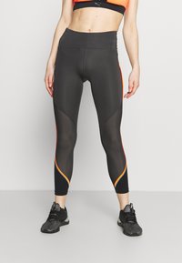 Höga svarta leggings med orange och vita detaljer, som har ett nätmönster på sidorna och en smidig, stretchy textur.