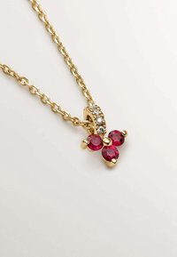 Collar de oro con un diseño de cadena, que presenta un colgante en forma de mariposa con tres piedras rojas redondas y strass transparentes sobre una base dorada.