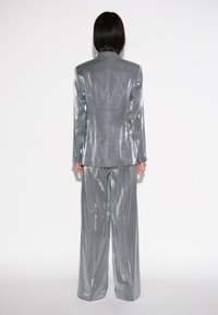 Metalen zilveren pak met een op maat gemaakte blazer en wijde broekspijpen, die een gladde, reflecterende textuur toont met een minimalistisch ontwerp.