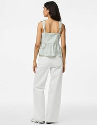 Top peplum de rayas claras con tirantes anudados, que presenta un espalda cuadrada y una cintura fruncida. Combinado con pantalones amplios blancos y zapatos negros.