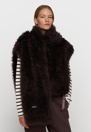 Gilet in finta pelliccia marrone scuro con colletto alto, caratterizzato da un design elegante. Maglietta a maniche lunghe a righe sottostante, con dettaglio del logo all'orlo.