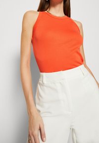 Top rosso senza maniche con scollo rotondo, abbinato a pantaloni bianchi a vita alta con una texture liscia e una vestibilità su misura.